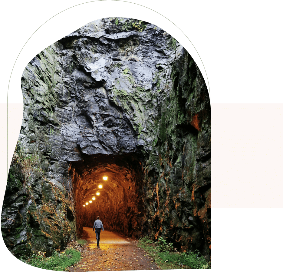 Person walking through lit tunnel in rocky cave, guided toward clarity by a San Francisco anxiety therapist.