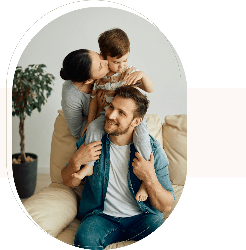 Smiling parents with child on shoulders at home, showing warmth through family counseling services in San Francisco.