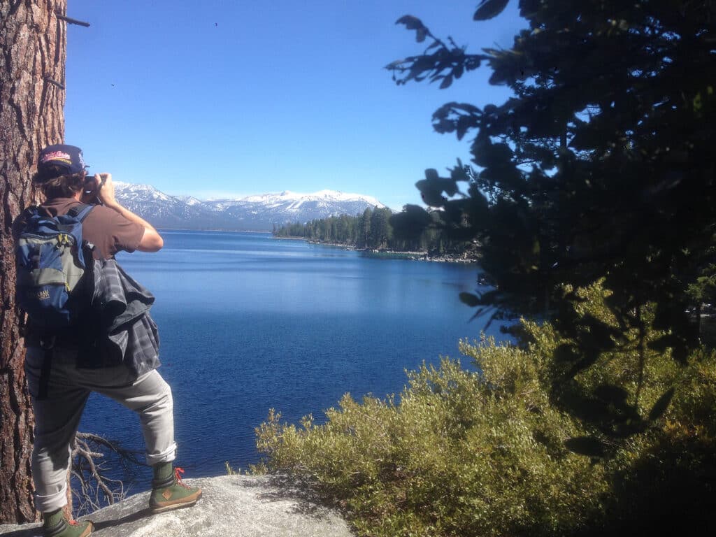 Man with backpack photographing lake and mountains, enjoying peace after anxiety therapy near San Francisco.