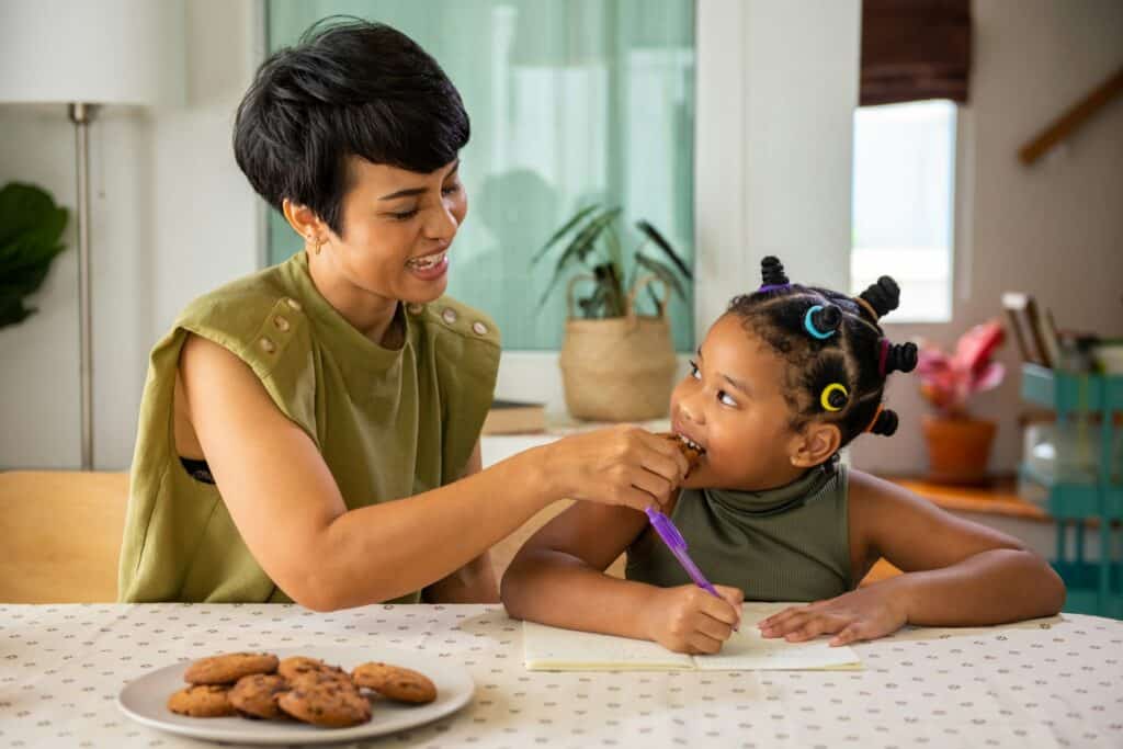 Mother feeding daughter while doing homework at home, reflecting support from CBT parent counseling San Francisco.